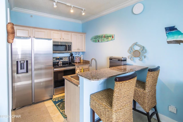 kitchen with dark stone countertops, appliances with stainless steel finishes, a breakfast bar, light tile patterned floors, and ornamental molding