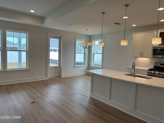 kitchen featuring pendant lighting, stainless steel appliances, sink, backsplash, and light stone counters