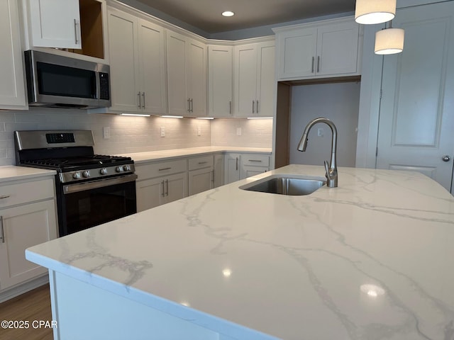 kitchen with appliances with stainless steel finishes, pendant lighting, white cabinetry, and sink