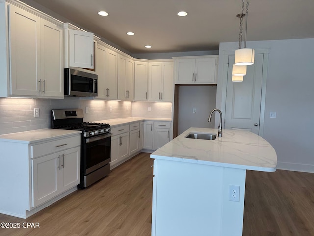 kitchen featuring pendant lighting, white cabinetry, stainless steel appliances, sink, and a center island with sink