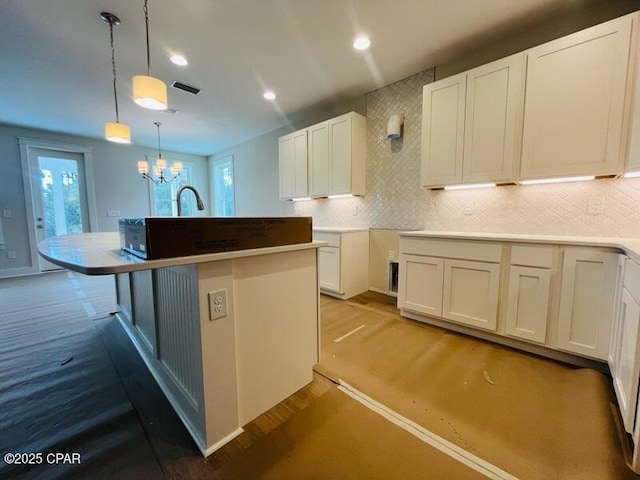 kitchen with white cabinets, a center island with sink, tasteful backsplash, decorative light fixtures, and a chandelier