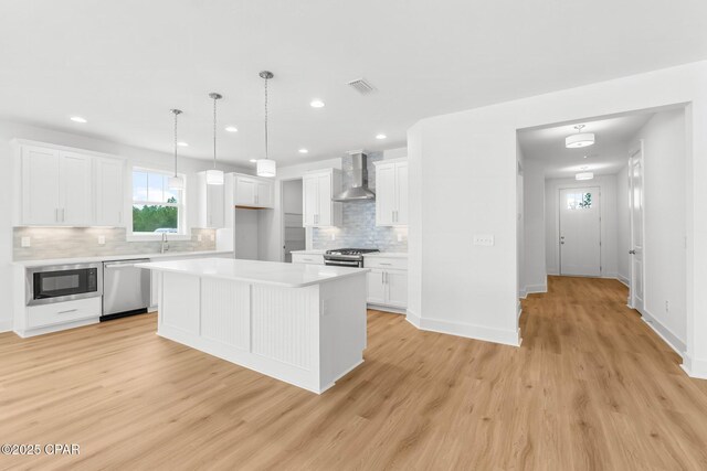 kitchen featuring stainless steel appliances, hanging light fixtures, wall chimney range hood, and white cabinets