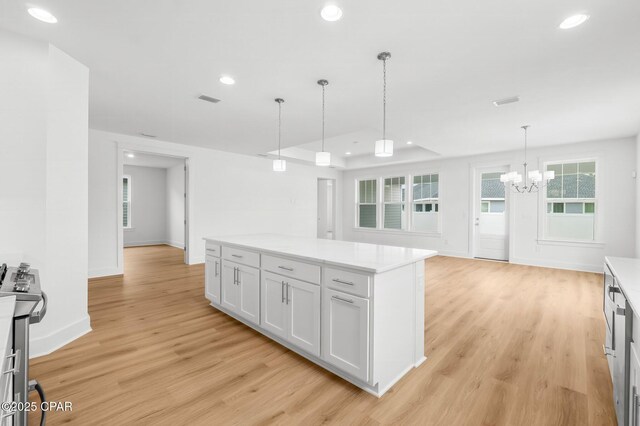 unfurnished living room featuring a chandelier, a raised ceiling, and light hardwood / wood-style floors