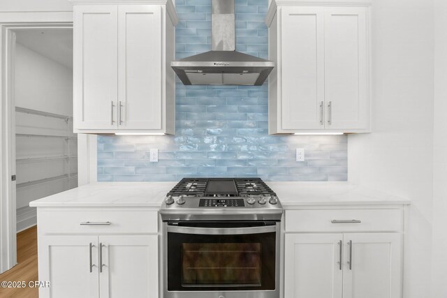 kitchen featuring wall chimney exhaust hood, stainless steel range with gas cooktop, and white cabinets