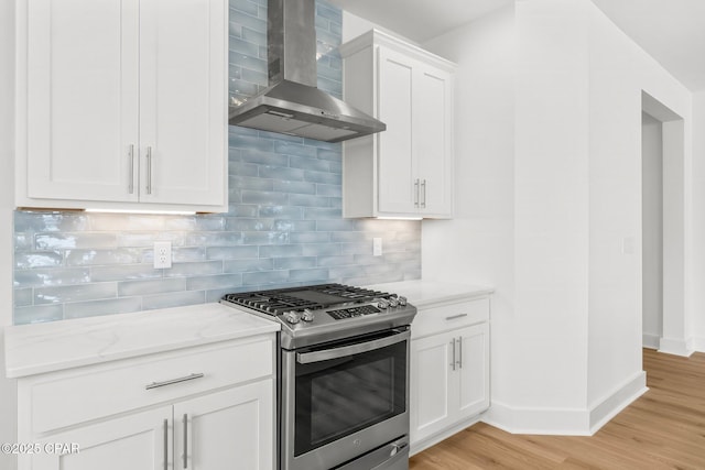 kitchen featuring backsplash, white cabinets, light stone counters, gas range, and wall chimney exhaust hood