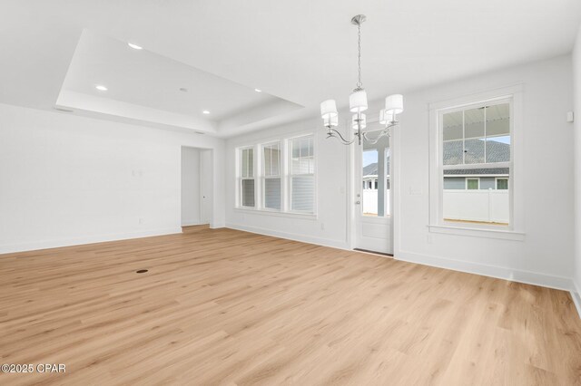 unfurnished dining area featuring an inviting chandelier, a tray ceiling, and light hardwood / wood-style floors