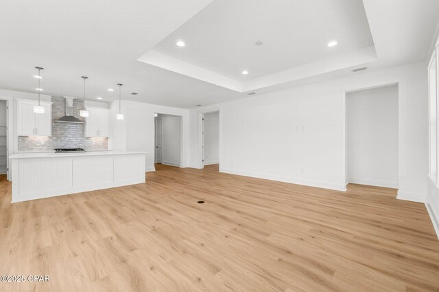 unfurnished living room with a raised ceiling and light wood-type flooring