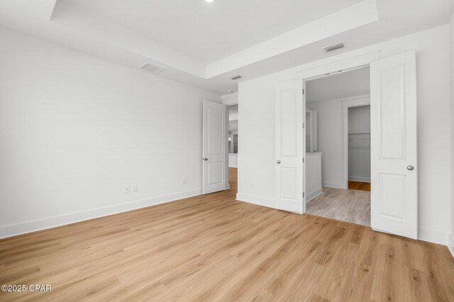 unfurnished bedroom with a raised ceiling and light hardwood / wood-style floors