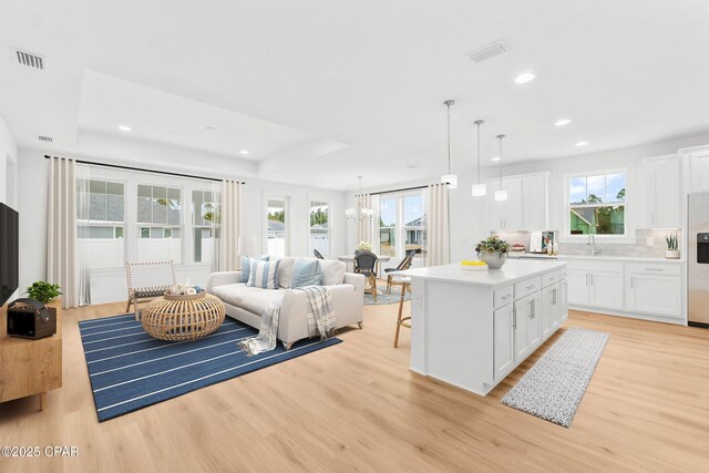 interior space with sink, a tray ceiling, a chandelier, and light hardwood / wood-style floors