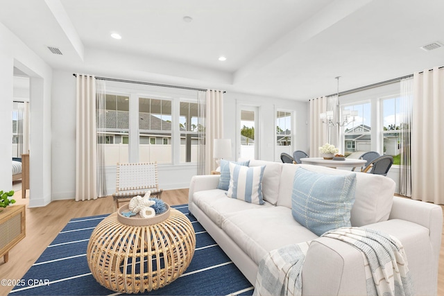 living room featuring a notable chandelier, light hardwood / wood-style floors, and a tray ceiling