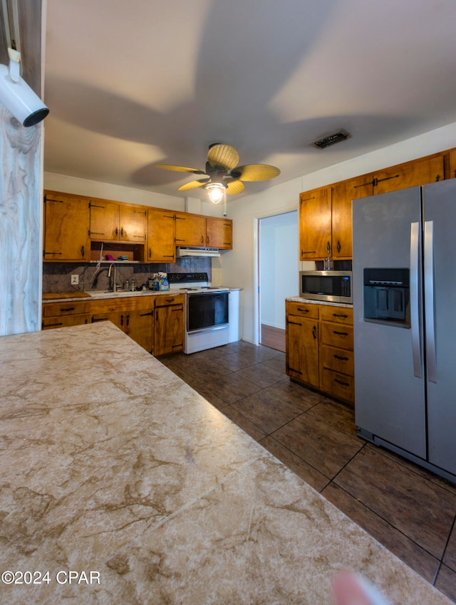 kitchen with stainless steel appliances, dark tile patterned flooring, decorative backsplash, sink, and ceiling fan