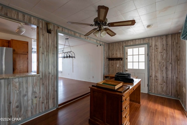 unfurnished office with wood walls, dark wood-type flooring, and ceiling fan