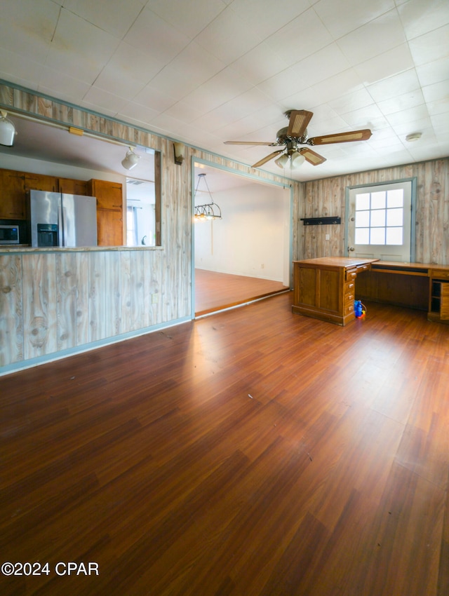 unfurnished living room with hardwood / wood-style floors, wood walls, and ceiling fan