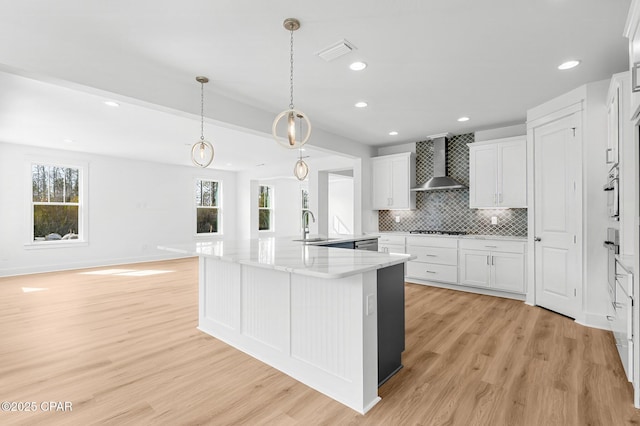 kitchen featuring wall chimney exhaust hood, sink, white cabinetry, light wood-type flooring, and kitchen peninsula