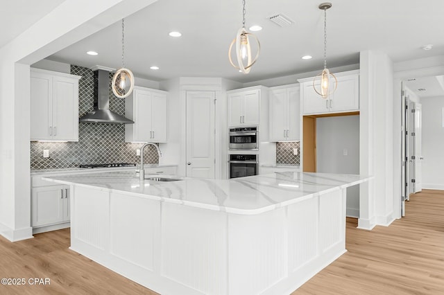 kitchen featuring pendant lighting, sink, wall chimney range hood, white cabinetry, and a spacious island