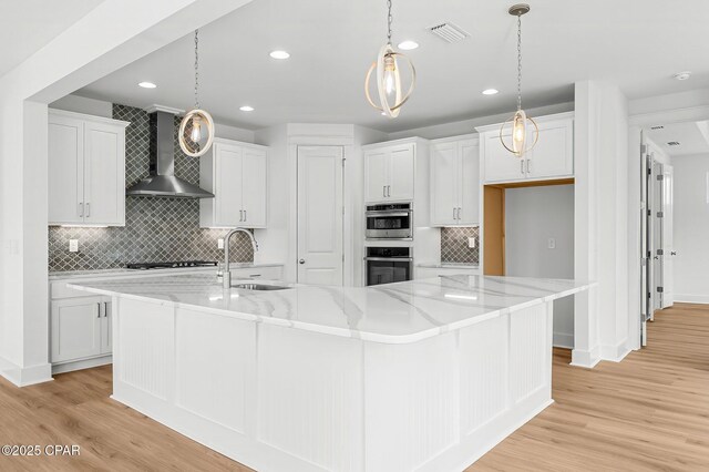 kitchen featuring pendant lighting, sink, wall chimney range hood, white cabinetry, and a spacious island