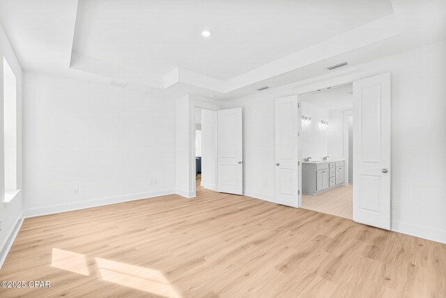 unfurnished bedroom featuring connected bathroom, light hardwood / wood-style floors, and a raised ceiling