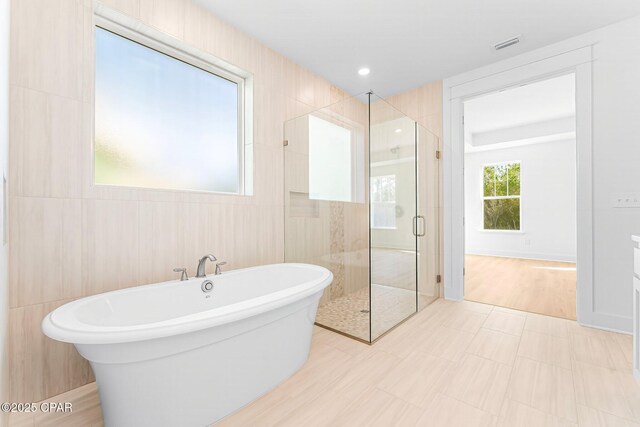 bathroom featuring shower with separate bathtub and tile walls