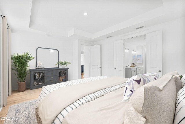 bedroom featuring ensuite bath, light hardwood / wood-style flooring, and a raised ceiling