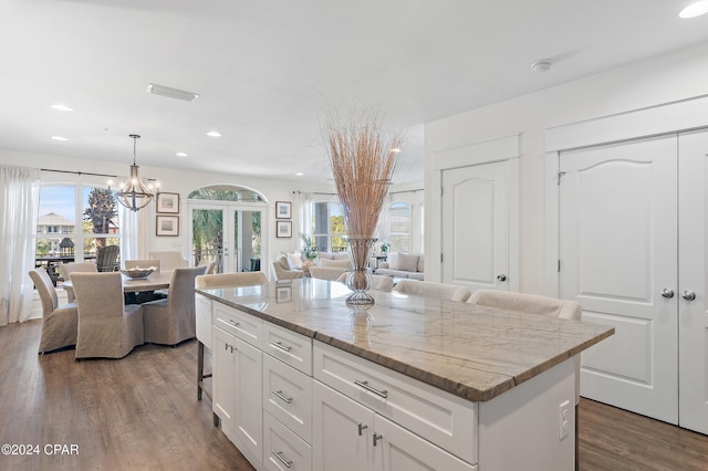 kitchen featuring light stone countertops, a breakfast bar, white cabinets, a kitchen island, and hanging light fixtures