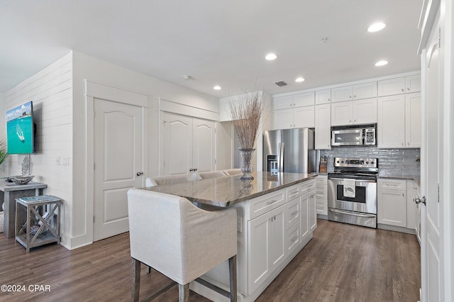 kitchen featuring a kitchen bar, appliances with stainless steel finishes, stone counters, white cabinets, and a kitchen island