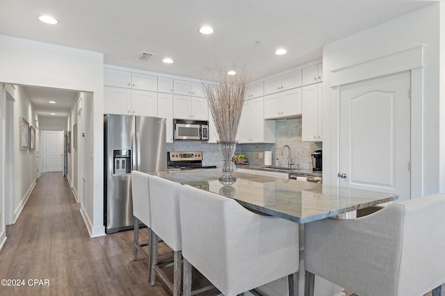 kitchen featuring a large island, stone countertops, a kitchen bar, white cabinets, and appliances with stainless steel finishes