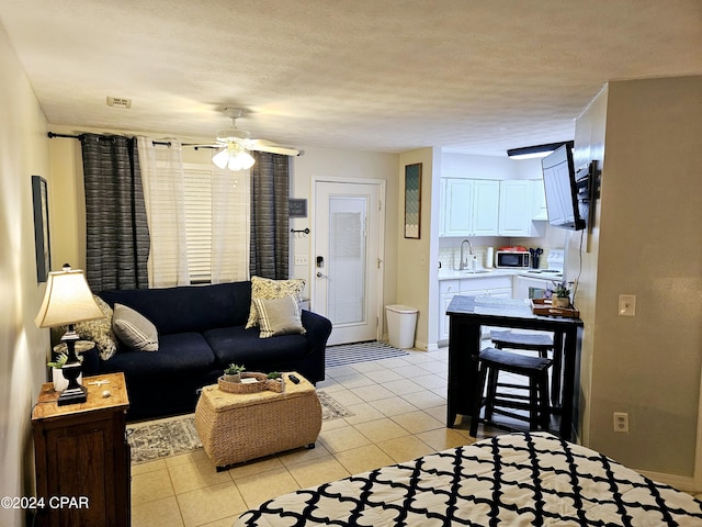 living room featuring sink, light tile patterned floors, a textured ceiling, and ceiling fan