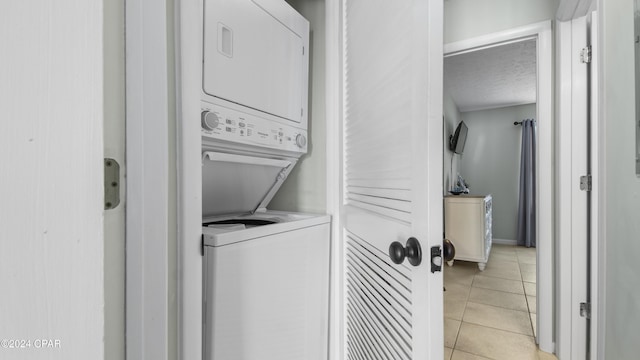 clothes washing area featuring light tile patterned floors, laundry area, stacked washer and clothes dryer, and a textured ceiling