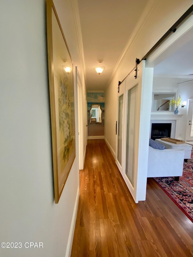 corridor featuring a barn door, wood-type flooring, and crown molding