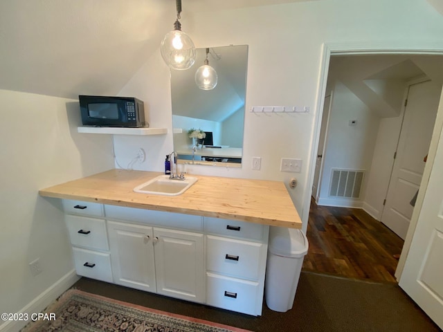 kitchen featuring butcher block counters, white cabinetry, sink, pendant lighting, and lofted ceiling