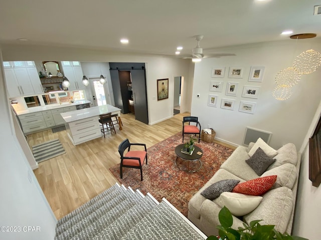 living room featuring ceiling fan, a barn door, and light hardwood / wood-style flooring