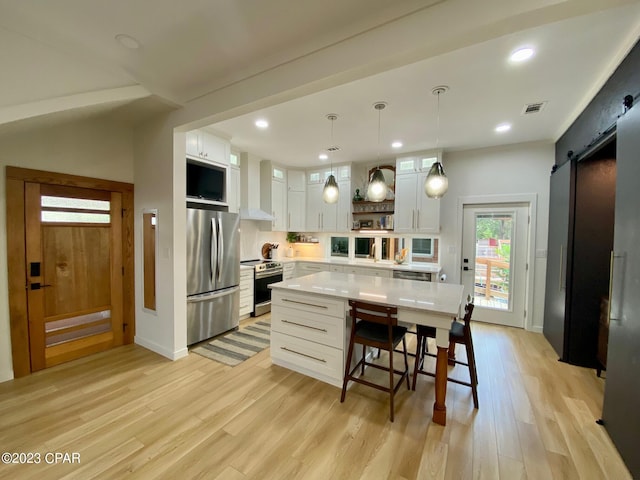 kitchen featuring appliances with stainless steel finishes, wall chimney range hood, a barn door, white cabinets, and a kitchen island