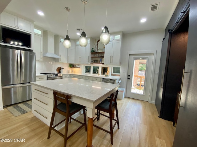 kitchen with white cabinetry, stainless steel appliances, wall chimney range hood, a barn door, and pendant lighting