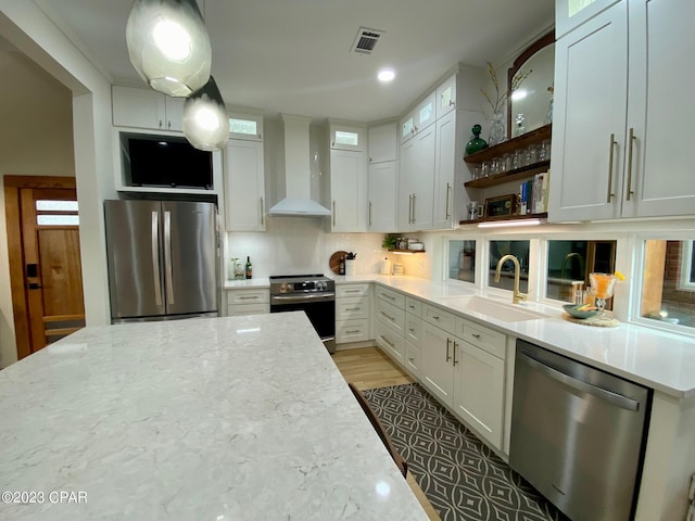 kitchen with white cabinets, wall chimney range hood, sink, light stone countertops, and appliances with stainless steel finishes