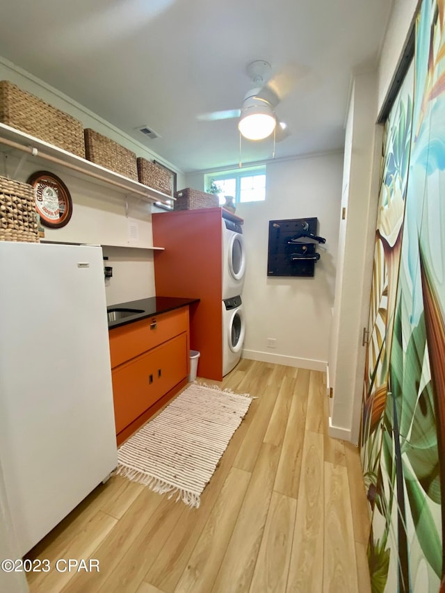 clothes washing area with ceiling fan, light wood-type flooring, and stacked washer / dryer