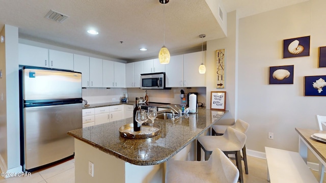 kitchen featuring stainless steel appliances, white cabinetry, hanging light fixtures, a breakfast bar, and dark stone countertops