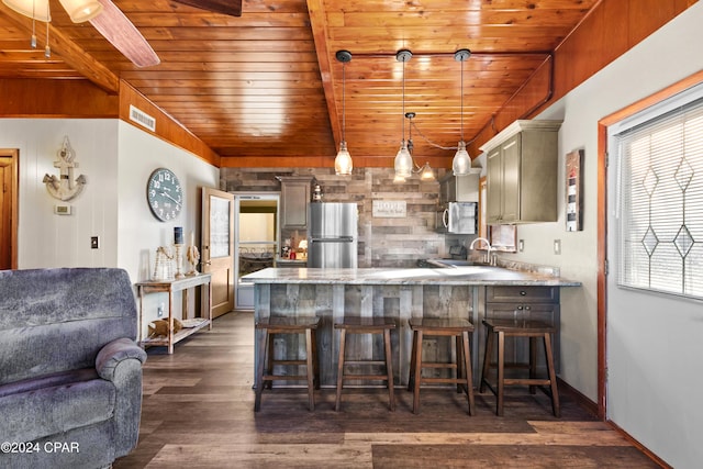 kitchen featuring hanging light fixtures, dark hardwood / wood-style floors, appliances with stainless steel finishes, a kitchen bar, and kitchen peninsula