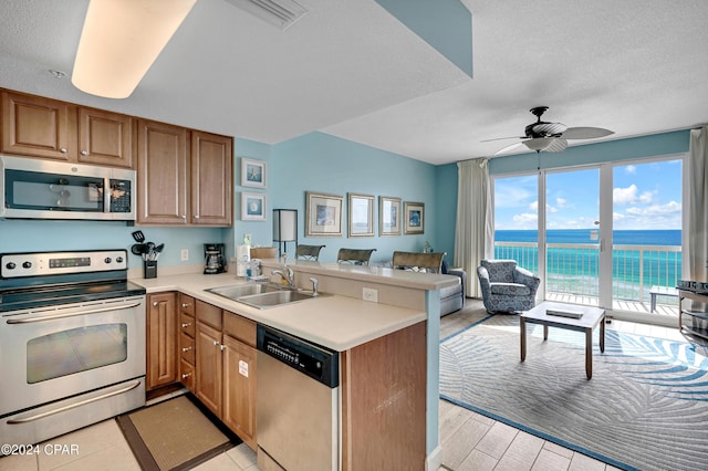 kitchen featuring kitchen peninsula, sink, appliances with stainless steel finishes, a textured ceiling, and a water view