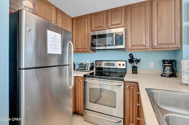 kitchen featuring a textured ceiling, light tile patterned floors, stainless steel appliances, and sink