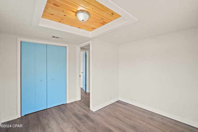 unfurnished bedroom with dark hardwood / wood-style floors, a tray ceiling, and a closet