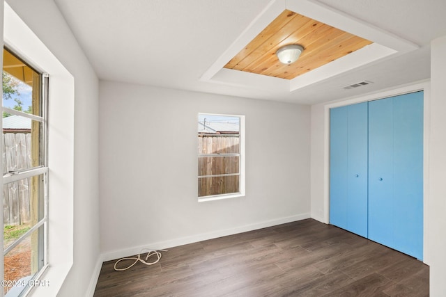 unfurnished bedroom with a tray ceiling, multiple windows, and dark hardwood / wood-style floors