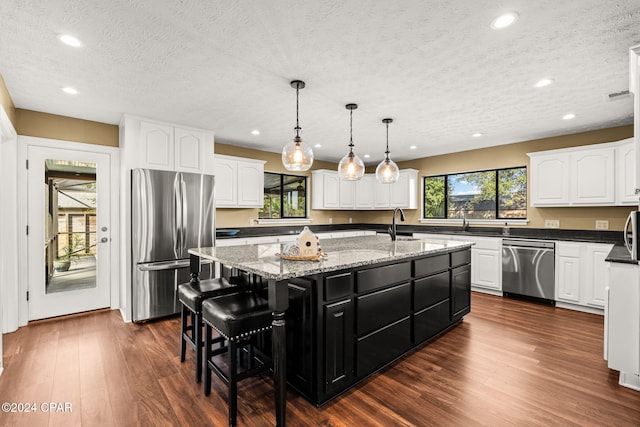 kitchen featuring appliances with stainless steel finishes, a textured ceiling, decorative light fixtures, dark hardwood / wood-style floors, and a center island