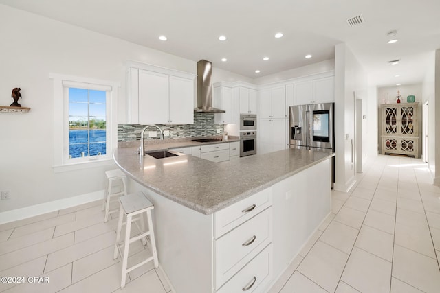 kitchen featuring white cabinets, decorative backsplash, sink, a kitchen breakfast bar, and wall chimney range hood