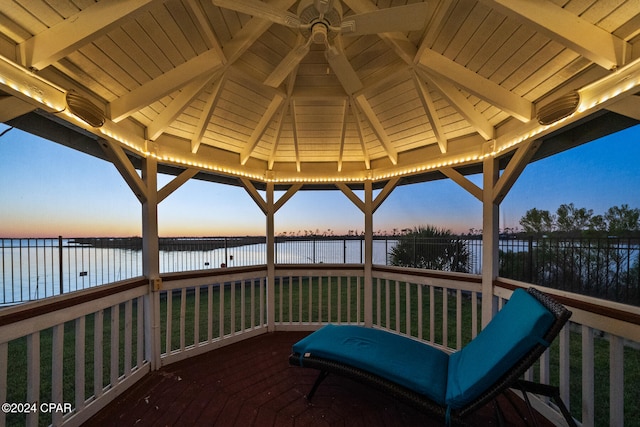 deck at dusk with a water view, a lawn, and a gazebo