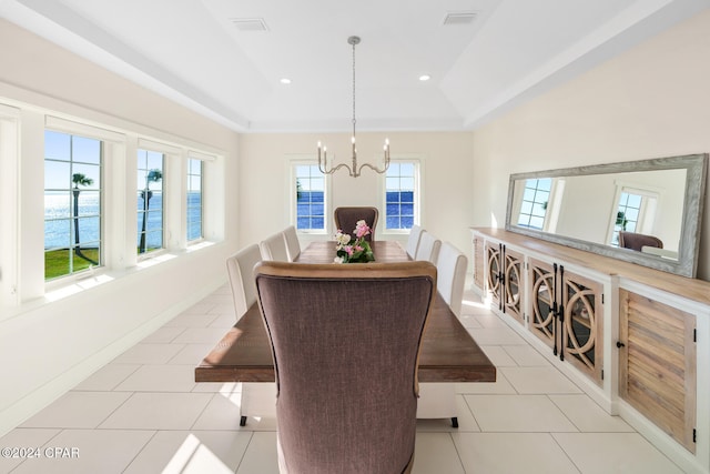 dining room with a chandelier, light tile patterned floors, a water view, and a raised ceiling