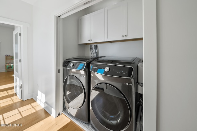 washroom featuring washing machine and clothes dryer, cabinets, and light hardwood / wood-style flooring