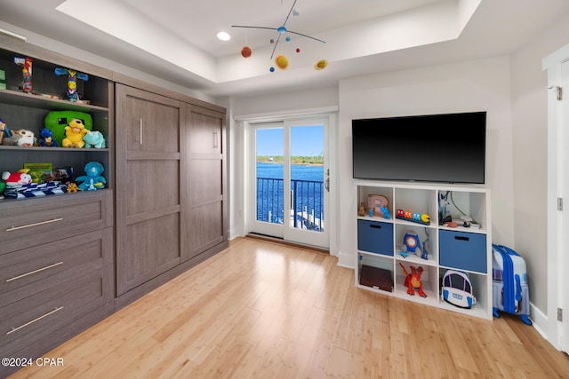 game room with light wood-type flooring and a raised ceiling