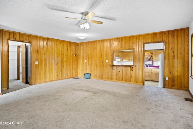 carpeted spare room featuring wood walls, ceiling fan, and a textured ceiling