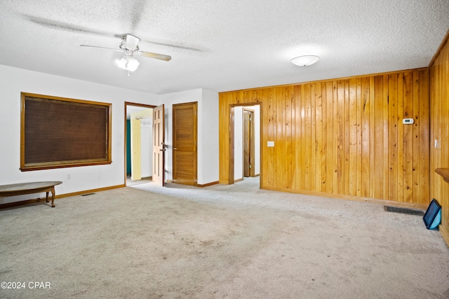 carpeted empty room featuring wood walls, a textured ceiling, and ceiling fan