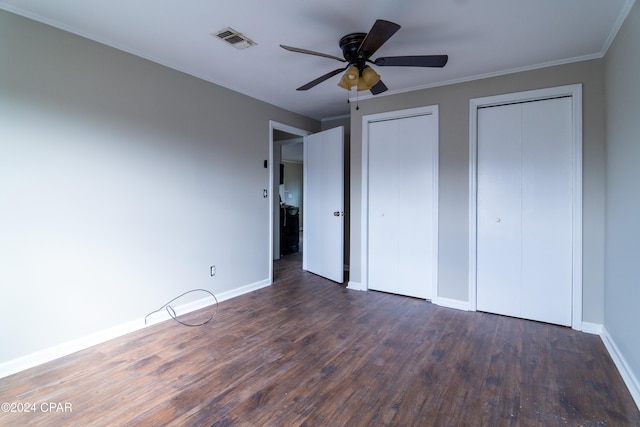 unfurnished bedroom with dark wood-type flooring, two closets, visible vents, and baseboards